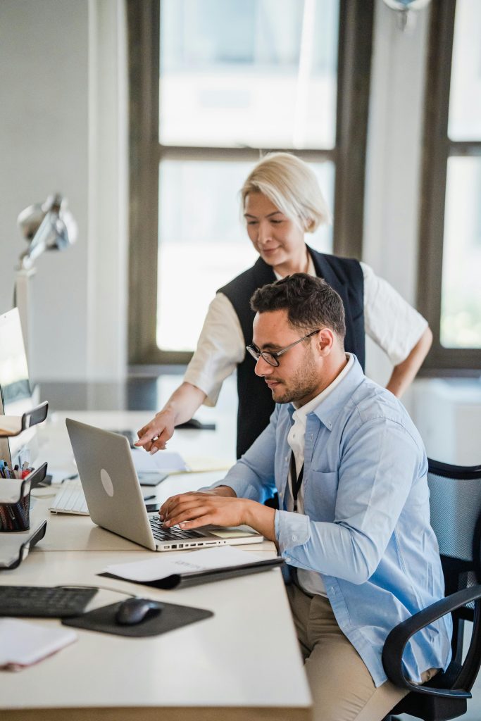 A man and woman collaborating on a project in a modern office with a laptop.