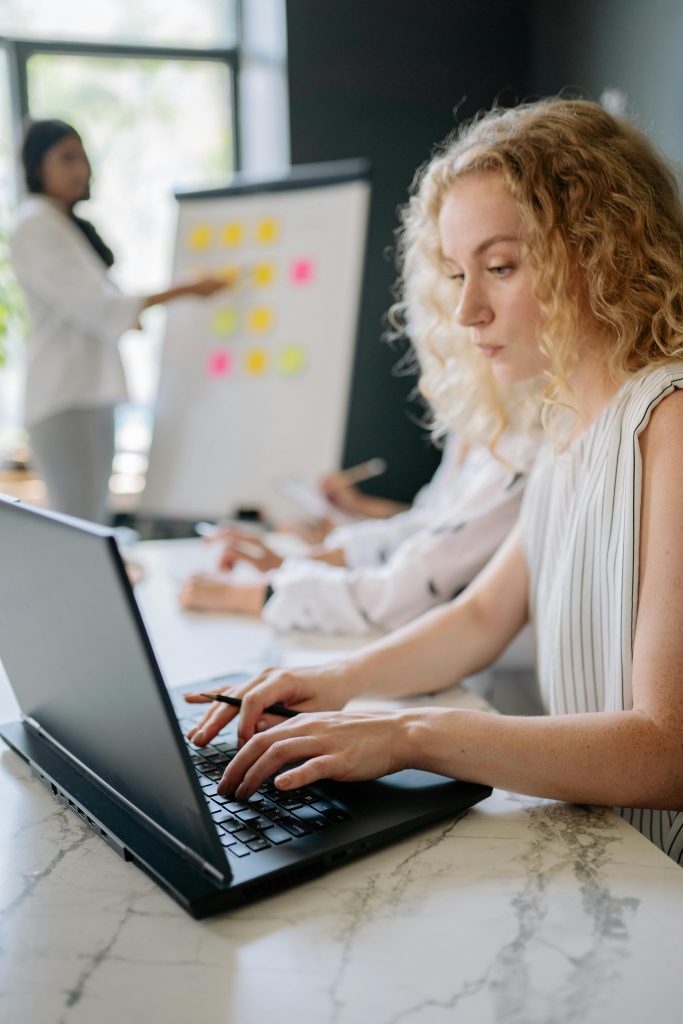 Focused woman typing on laptop during a collaborative business meeting with a presentation.