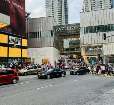 Vibrant street view of Pavilion Kuala Lumpur, showcasing urban life with cars and pedestrians.