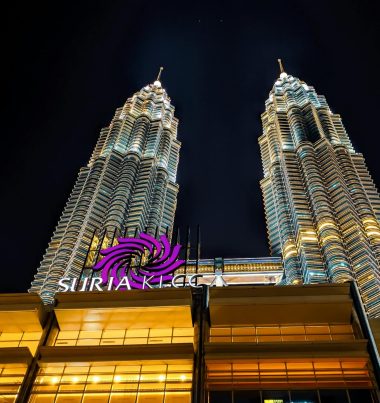 The illuminated Petronas Towers dominate Kuala Lumpur's skyline at night. Stunning low angle view.