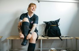 A female soccer player laughing while putting on boots in a locker room.